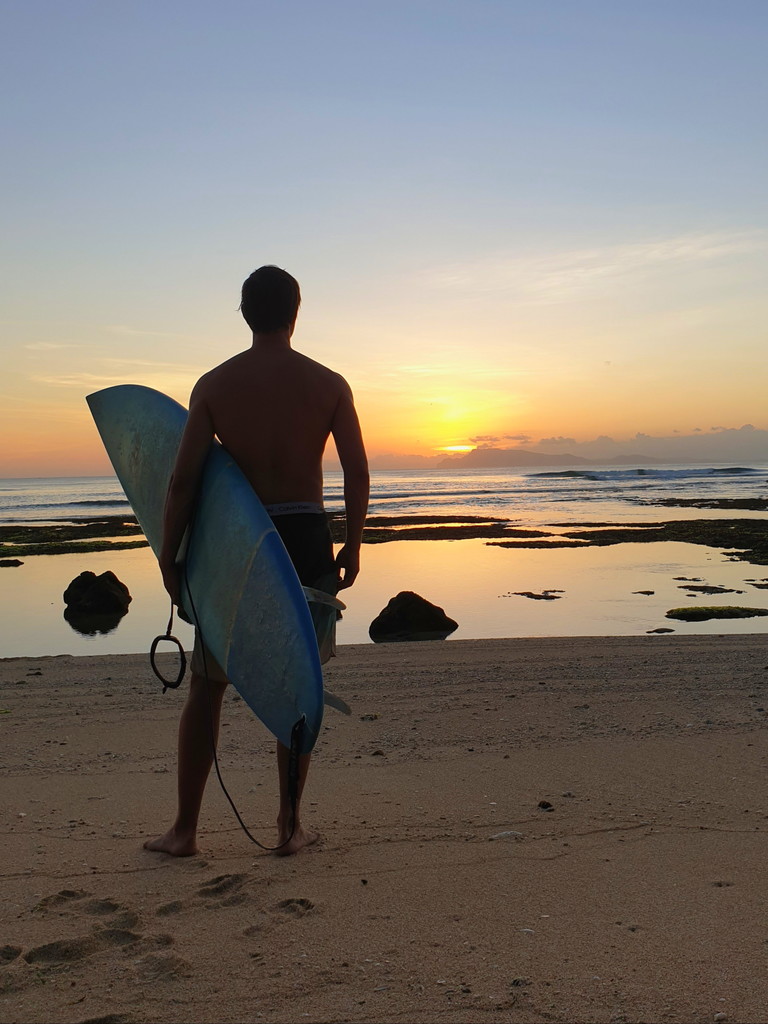 Surfer standing on beach at sunset